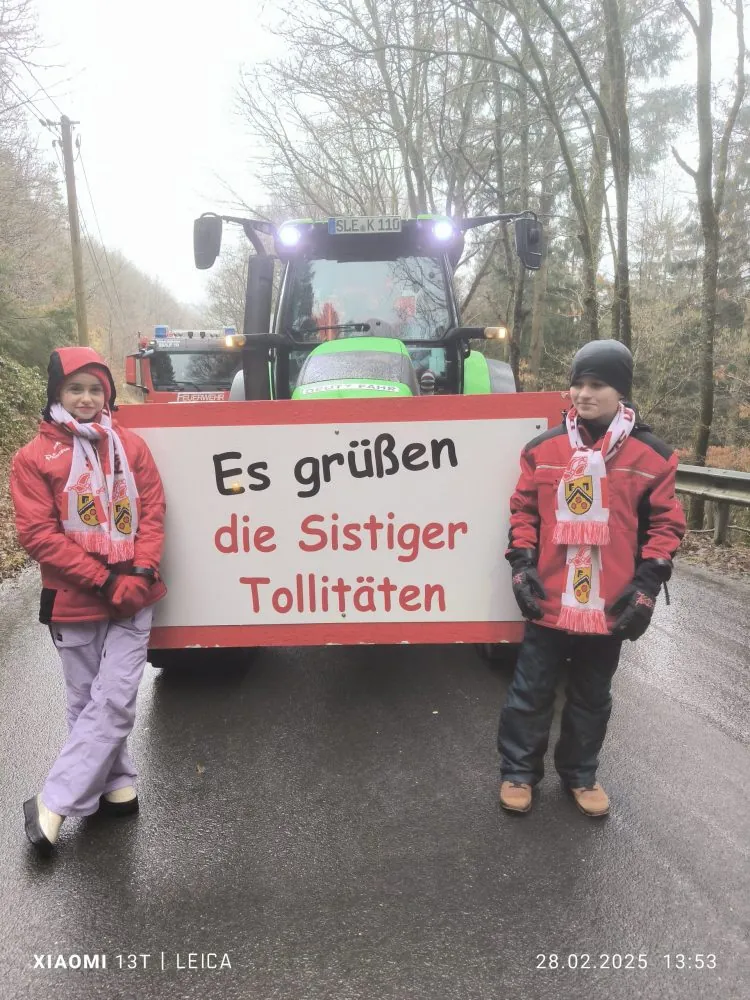 Zwei Personen vor einem Traktor mit dem Schild „Es grüßen die Sistiger Tollitäten“